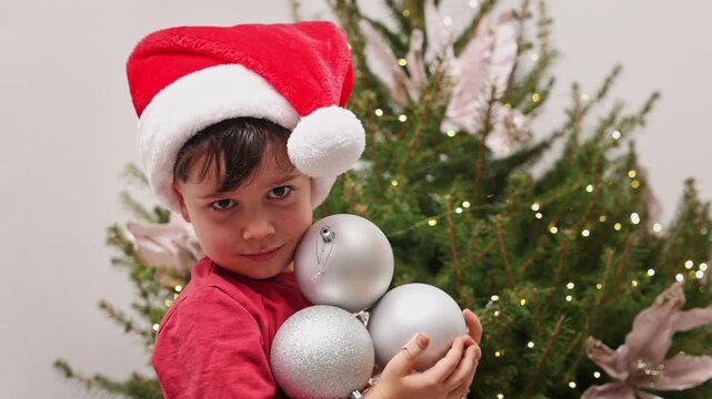 Close-up shots of two boys and their grandmother decorating a Christmas tree indoors. The brothers wear festive hats and pet a black cat near winter ornaments and a toy snowman.
