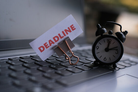 "Deadline" text and a small alarm clock on a laptop keyboard. Deadline and work concept with text on an alarm clock on a desk. Motivation and management. Racing against time. Working under pressure.