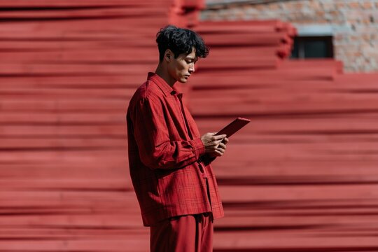 Young man in red outfit using tablet at industrial lumber yard for fashion editorial and digital workflow background scene