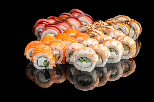Assorted sushi rolls arranged in a colorful display on a reflective black surface showcasing various ingredients and styles including salmon, tuna, and eel