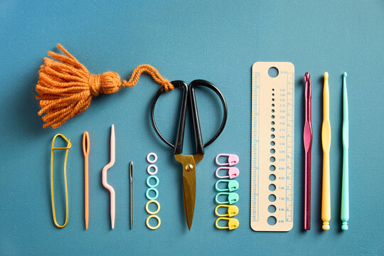 A collection of colorful knitting and crochet tools neatly arranged on a blue background, with yarn, needles, hooks, scissors and accessories for creative textile crafts.