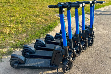 Several electric scooters parked in a row on a path with a green grass background © ir1ska