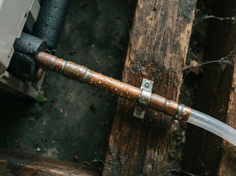 Copper pipe clamped to a weathered post dripping beside a cooling unit