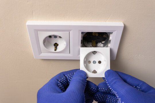 Close-up: an electrician holds a socket cover in both hands, preparing to replace it with a new one.