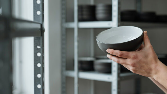 person holding ceramic bowl in warehouse shop with shelves background