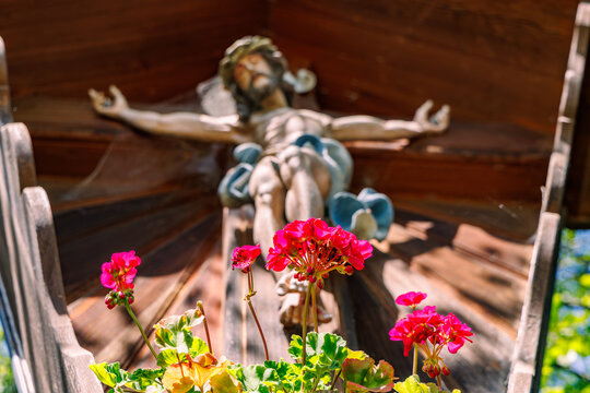 Pink red geranium flowers in front of traditional wooden carved crucifix at roadside shrine, Bavarian religious folk culture and Christian faith concept