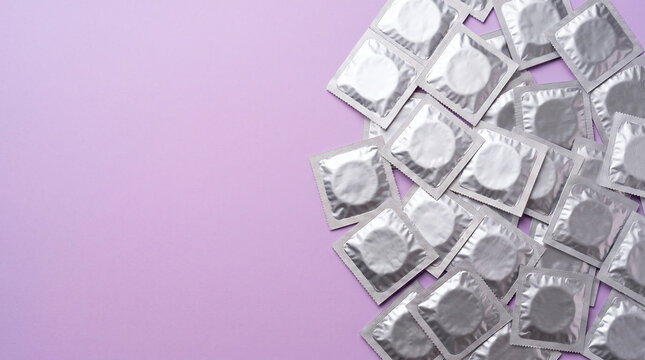 Silver condom wrappers arranged on a soft purple background with ample copy space for text