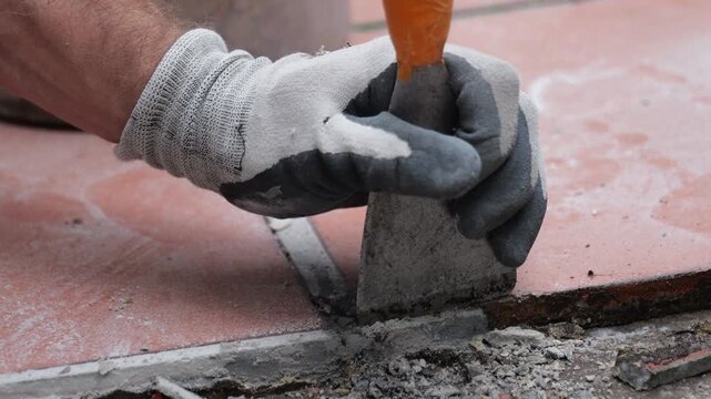 Gloved hand chiseling old ceramic tile during floor repair work