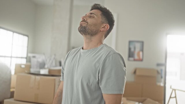 Man surrounded by packed cardboard boxes and bubblewrap, head tilted back and sighing in a building; moving exhaustion.
