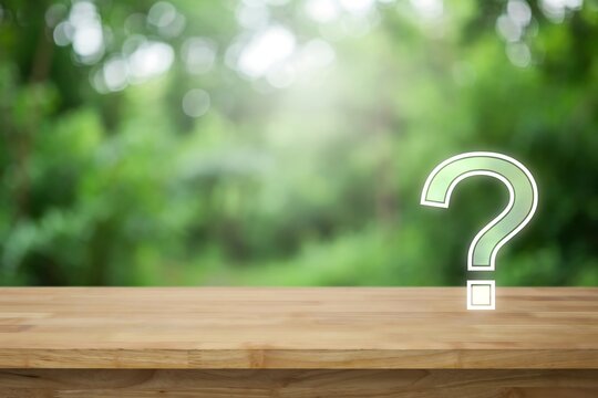 Question mark icon floating above a wooden table with a blurred green forest background and copy space