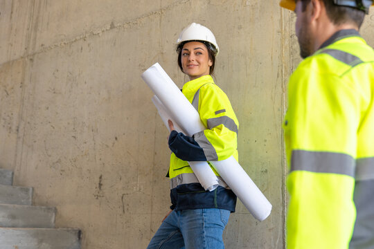 Smiling female architect holding paper blueprints near colleague