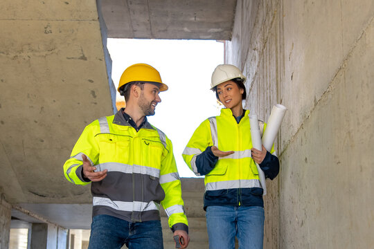 Man and woman construction workers talking while walking with plans