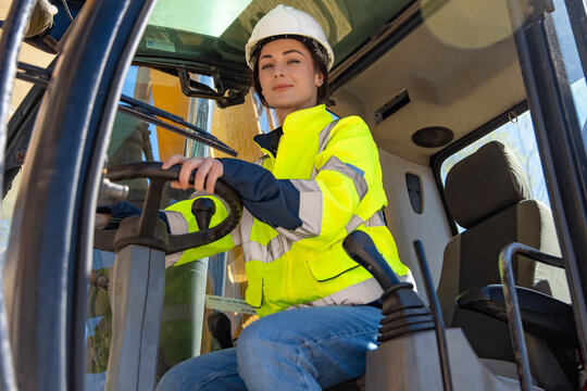 Female machine operator sitting inside excavator cabin looking at camera
