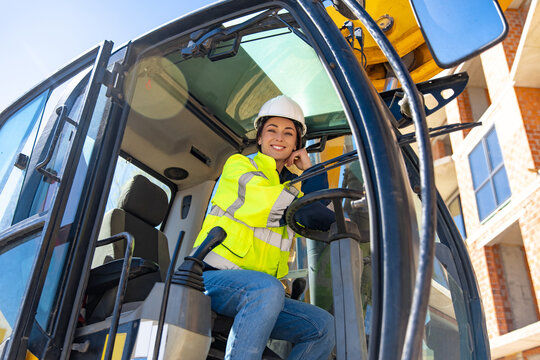 Smiling female excavator operator leaning on hand inside vehicle cabin