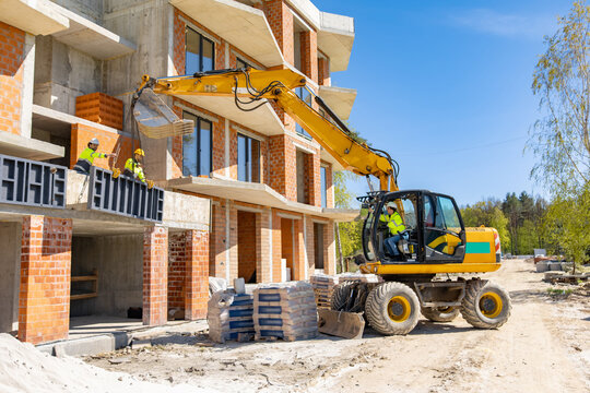 Construction workers lifting heavy metal panel with excavator bucket