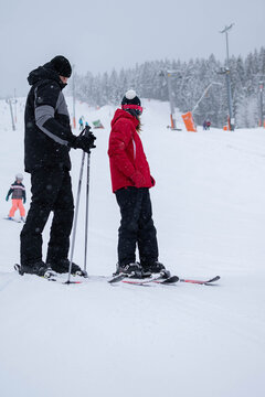 A father helps a child practice skiing together on a snowy slope at a winter resort. The scene represents ski instruction, parental support, childhood learning, and family recreation.