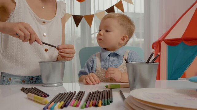 A mother and her young child are engaged in a fun learning activity as they sharpen colored pencils. They explore colors and enjoy creative playtime in a bright space.