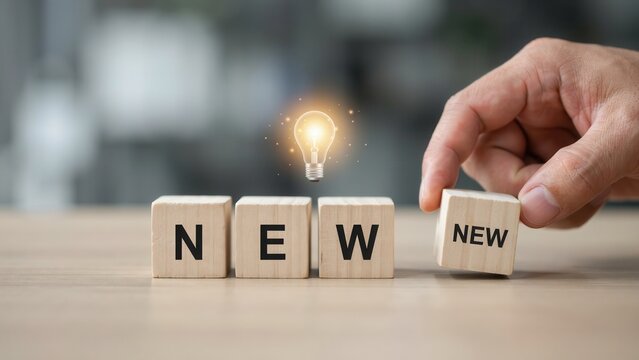 Hand completing 'NEW' word with wooden blocks and glowing light bulb concept