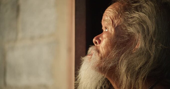 A rural senior man with a long white beard steps to an open door, gazing out at the last light of dusk before sunset.
