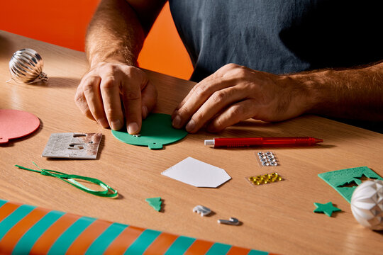 Man crafting handmade Christmas decorations and gift tags at wooden table