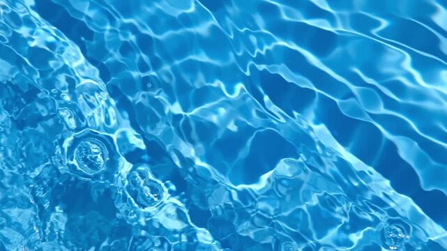Clear blue swimming pool water surface with moving ripples, waves, reflections, and shimmering sunlight patterns. 