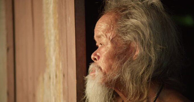 A rural senior man with a long white beard steps to an open door, gazing out at the last light of dusk before sunset.