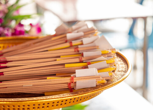 Bundles of incense sticks and candles wrapped in paper on woven tray, traditional Buddhist worship ritual set