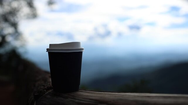 Black Coffee Cup on a Wooden Bench with Dramatic Mountain and Cloudy Sky
