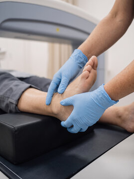 commercial medical close-up of a technician's gloved hands carefully positioning a patient's lower leg and foot for a bone density DEXA scan, clean clinical atmosphere, premium healthcare photo