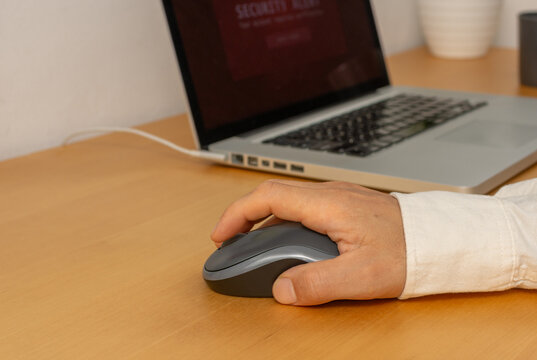 Close up of hand about to click computer mouse with laptop in background