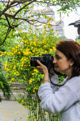 woman with red hair holds black digital camera near eye, profile, portrait, close-up, mirrorless, middle age, lens mounted, greenery in background, green plants, beautiful, romance, white blouse, take © Studio  GULL