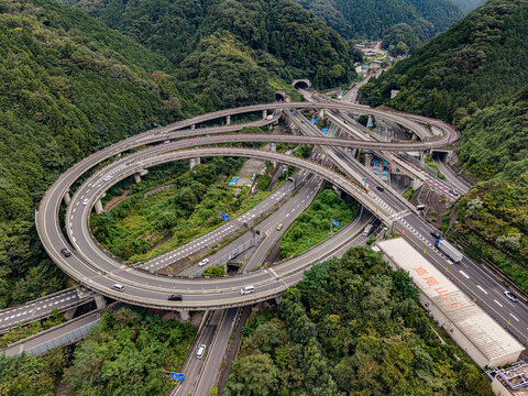 Aerial view of the Takaosan Interchange featuring complex looping highway ramps surrounded by dense green forest and mountainous terrain Hachioji, Tokyo, Japan.