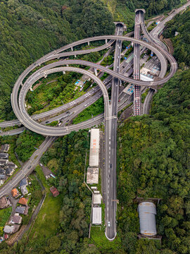 Aerial view of Takaosan toll gate and the complex highway interchange with looping ramps surrounded by dense green forest in Hachioji, Tokyo, Japan.