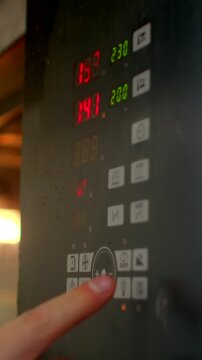 close up view of hand pressing appliance control dial and square function buttons, revealing red and green led digits on glossy black panel for heating settings