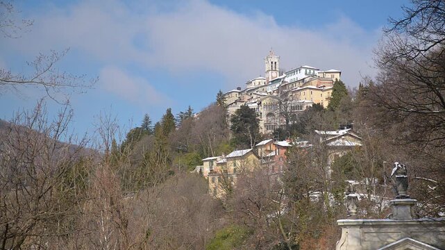 Panorama of Sacro Monte di Varese UNESCO village from the eleventh chapel, bell tower skyline, winter snow, blue sky and fast moving clouds, Santa Maria del Monte, Italy