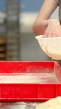 closeup of hand pinching and sprinkling fine flour powder above glossy red tray on indoor kitchen countertop, with hand, sprinkle, powder, flour detail, with