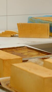 close-up view of rectangular sponge loaves staged on metal trays and white prep table showing neatly stacked even slices beside partially wrapped loaf with cake