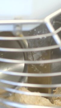 vertical close-up looking through curved cage bars at indoor pet enclosure with dark textured wheel and bedding substrate, captured from above soft warm light