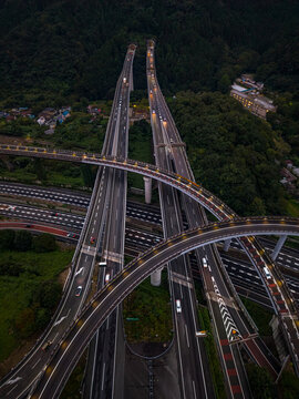 Aerial view of Hachioji JCT with illuminated highway ramps, flowing traffic, and surrounding dense forest in Hachioji, Tokyo, Japan.