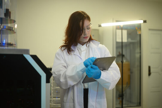 Caucasian Female Scientist Using Digital Tablet in Modern Laboratory Wearing Lab Coat and Safety Glasses