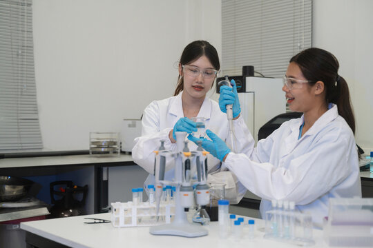 Two Young Asian Female Scientists Working Together in Laboratory Using Pipette and Test Tubes