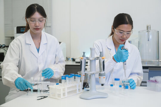 Two Asian Female Scientists Working in Modern Laboratory with Pipettes and Test Tubes