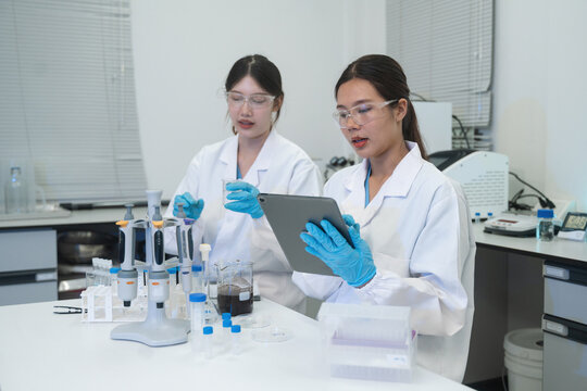 Two Asian Female Scientists Working in Laboratory with Tablet and Pipette Equipment