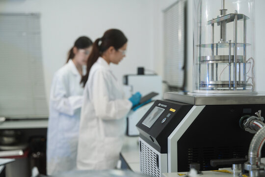Selective focus of Freeze Dryer Equipment with Two Female Scientists Working on Modern Research Laboratory Background