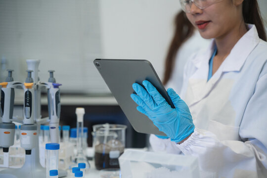 Close up of Female Scientist Using Digital Tablet in Laboratory with Pipettes and Test Tubes