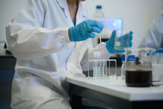 Cropped image of Scientist in White Lab Coat and Blue Gloves Pipetting Liquid into Test Tubes in Modern Laboratory
