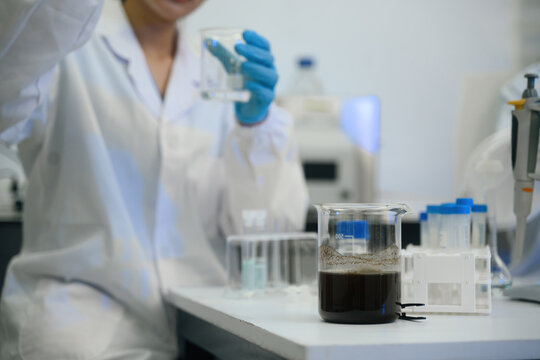 Close up of Scientist Analyzing Dark Liquid Sample in Laboratory Beaker with Gloves and Lab Coat