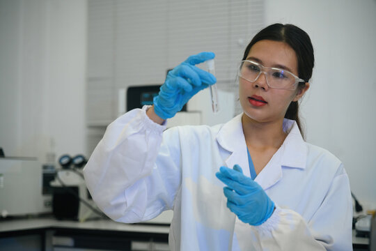 Close up of Asian Female Scientist Examining Test Tube in Modern Laboratory with Safety Glasses and Gloves