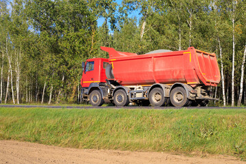 Red truck loaded with crushed stone on a forest road. © yaviki