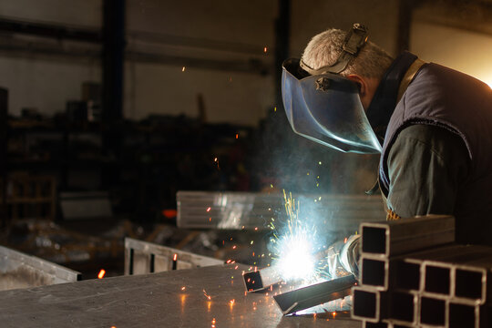 Metal pieces in foreground with welder working and sparks